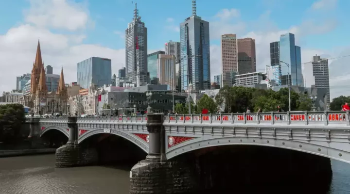 The image depicts the skyline of Melbourne, Australia. Prominent modern skyscrapers are visible in the background, showcasing the city's architectural diversity.
