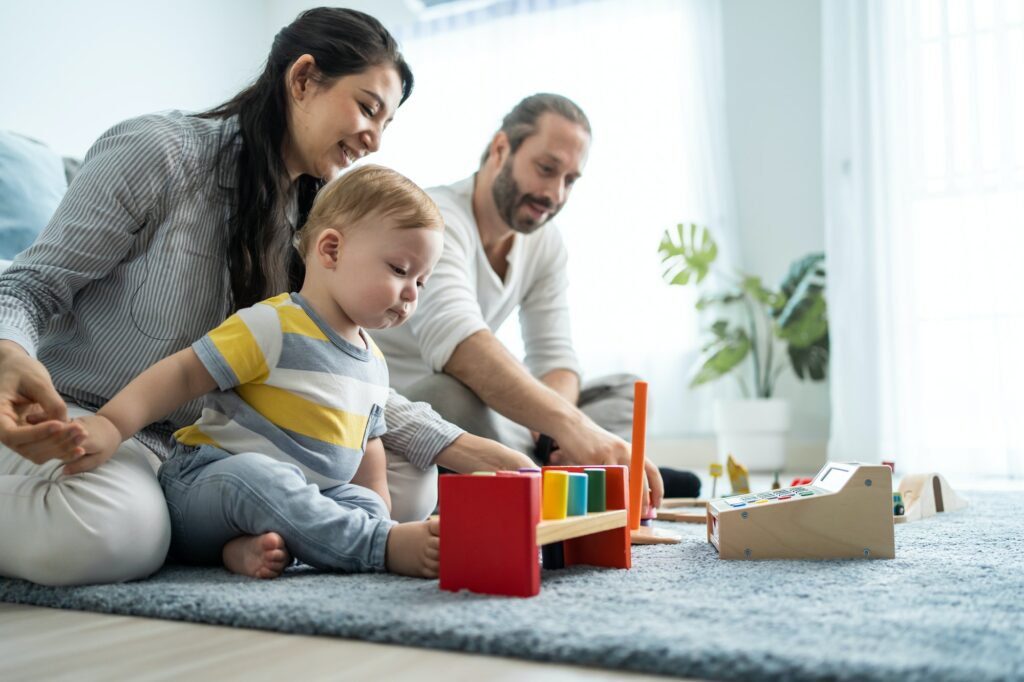 Caucasian happy loving parent play with baby toddler in living room.