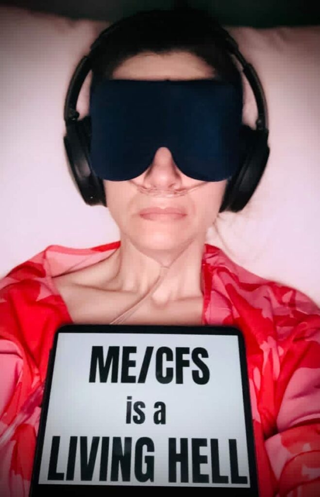 Rosalyn is holding a sign that reads: ME/CFS is a living hell.