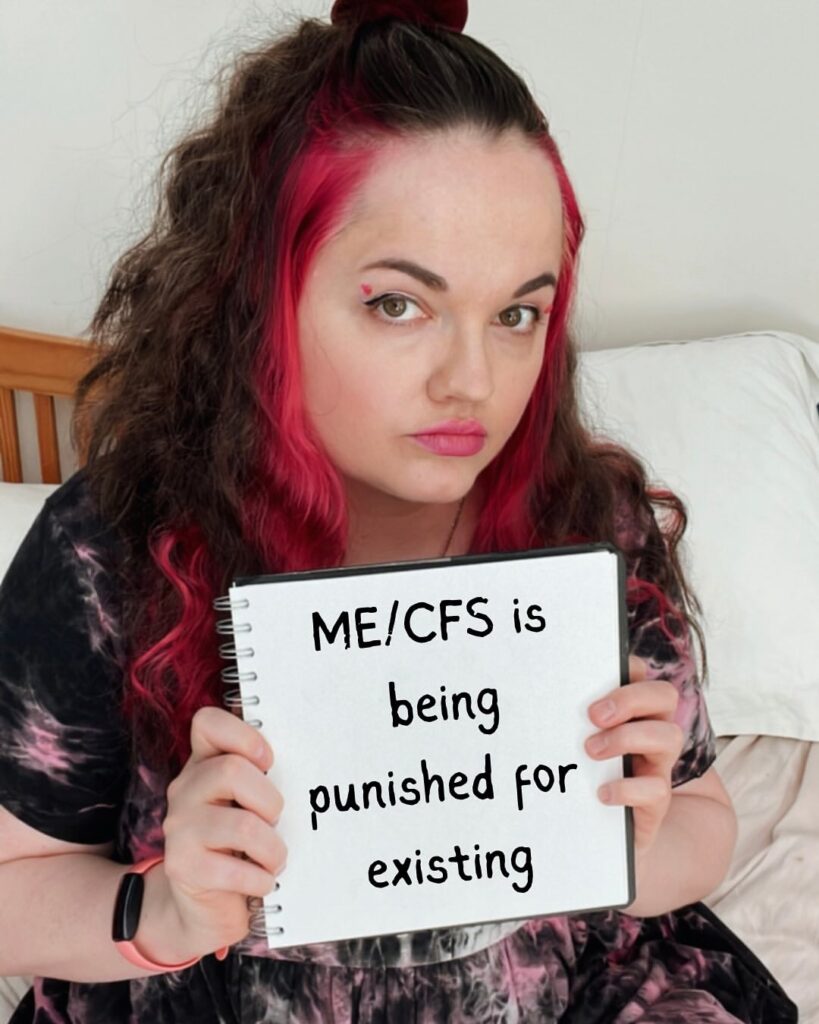 Fran is holding a sign that reads: ME/CFS is being punished for existing.
