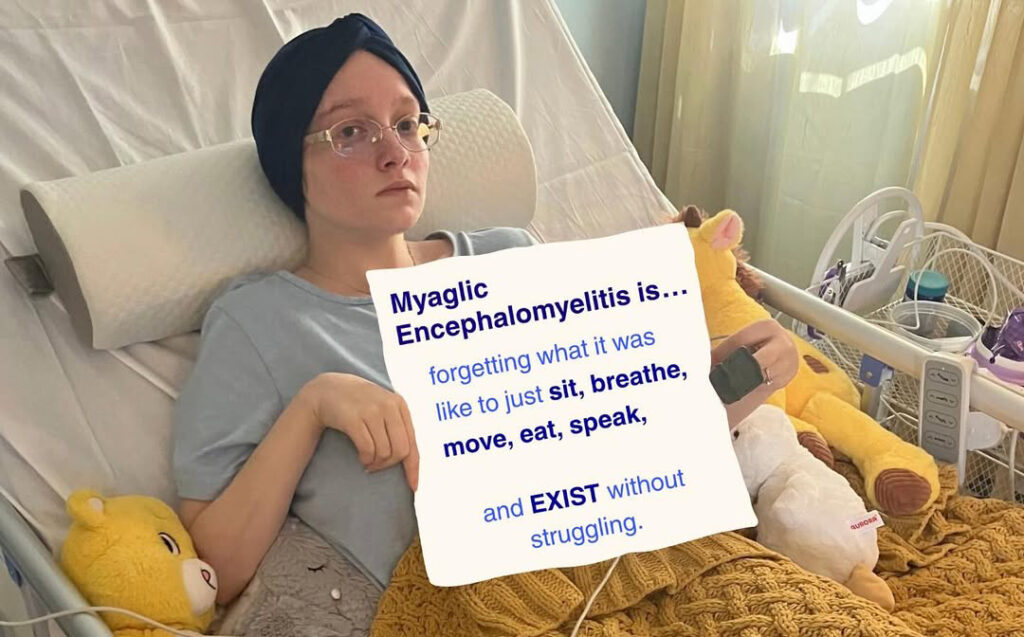 Em is holding a sign that reads: Myalgic Encephalomyelitis is forgetting what it was like to just sit, breathe, move, eat, speak, and EXIST without struggling.